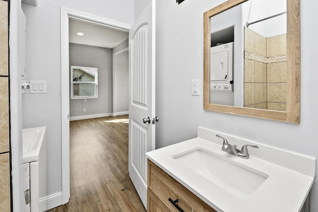 bathroom featuring stacked washer and dryer, baseboards, wood finished floors, and vanity