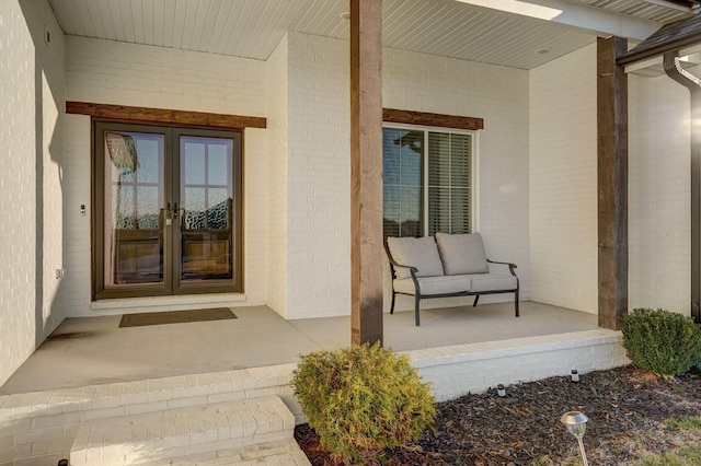 view of exterior entry with covered porch, french doors, and brick siding