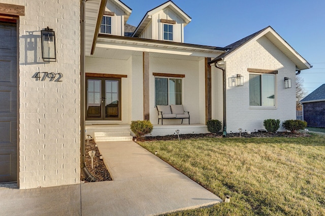 entrance to property featuring french doors, brick siding, a yard, and covered porch