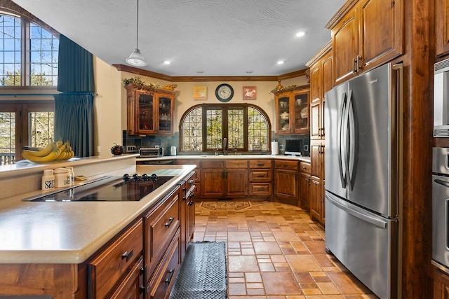 kitchen with stainless steel appliances, stone tile flooring, light countertops, brown cabinetry, and glass insert cabinets