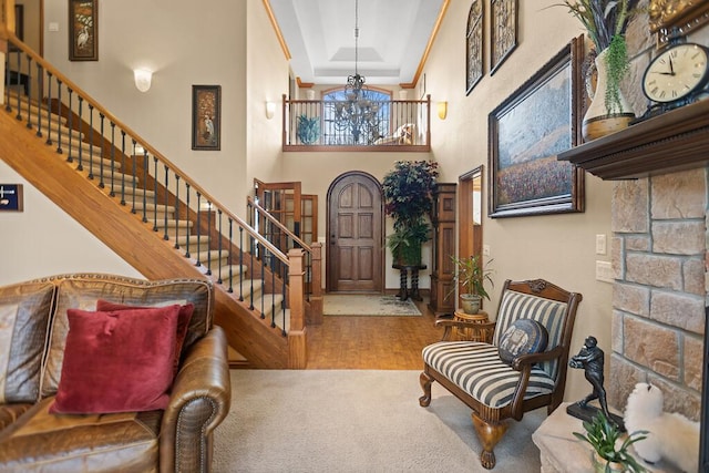 entrance foyer with carpet, a raised ceiling, stairway, a high ceiling, and a chandelier