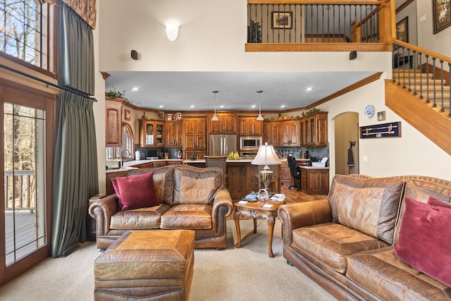 living room featuring light carpet, arched walkways, a towering ceiling, stairway, and ornamental molding