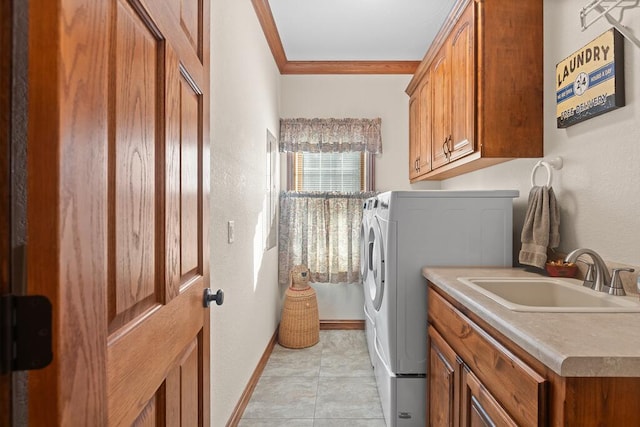 washroom featuring crown molding, washer and clothes dryer, cabinet space, a sink, and baseboards