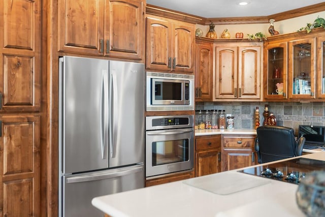 kitchen featuring tasteful backsplash, light countertops, appliances with stainless steel finishes, brown cabinetry, and glass insert cabinets