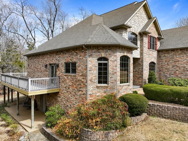 view of side of home with a patio area, a shingled roof, brick siding, and a wooden deck