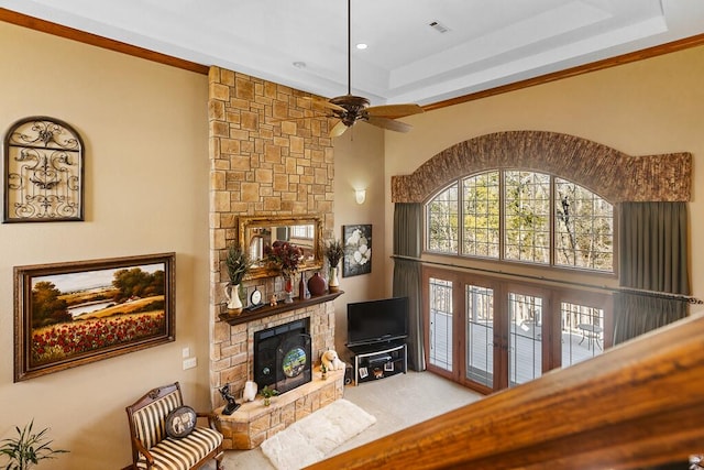 living room with a stone fireplace, a high ceiling, carpet flooring, visible vents, and a tray ceiling