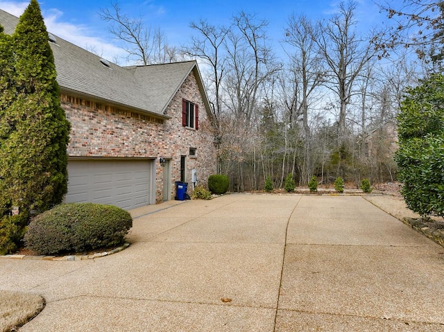 view of property exterior with driveway, a shingled roof, an attached garage, and brick siding