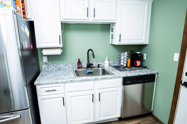 kitchen featuring stainless steel appliances, wood finished floors, a sink, and white cabinetry