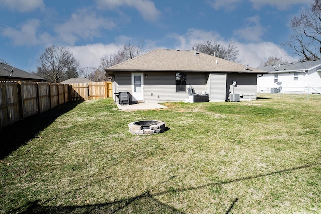 rear view of property with central air condition unit, a shingled roof, a lawn, a fenced backyard, and a fire pit