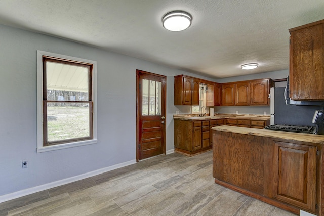 kitchen with light countertops, brown cabinetry, a textured ceiling, a peninsula, and baseboards