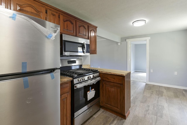 kitchen with a textured ceiling, stainless steel appliances, a peninsula, and baseboards