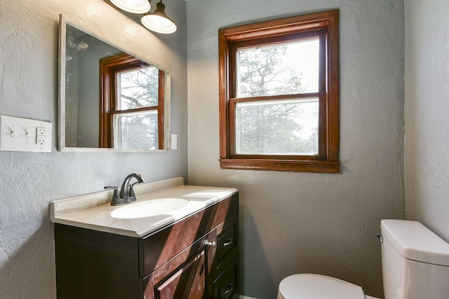 bathroom with a textured wall, vanity, and toilet