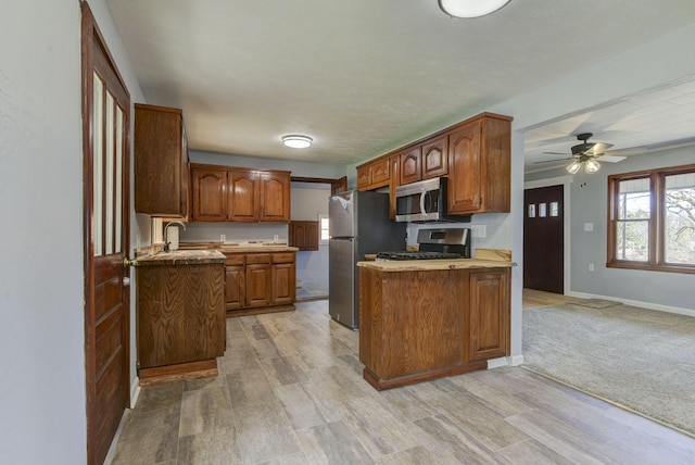 kitchen featuring a peninsula, a sink, baseboards, appliances with stainless steel finishes, and brown cabinetry