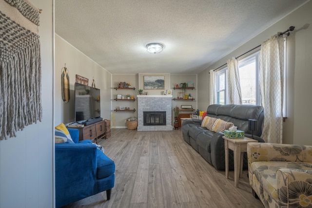 living area with a textured ceiling, a brick fireplace, and light wood-style floors