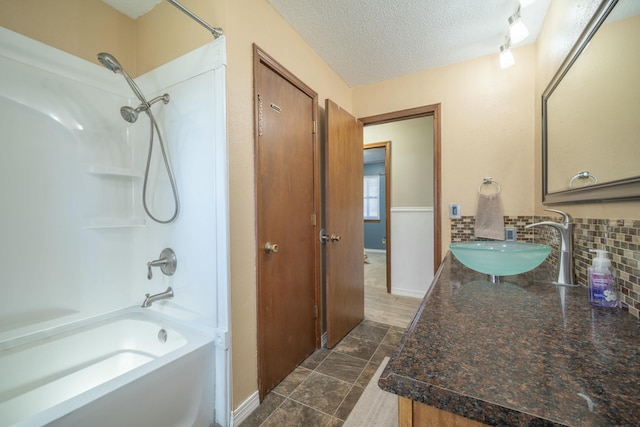 bathroom featuring baseboards, decorative backsplash, a textured ceiling, vanity, and washtub / shower combination