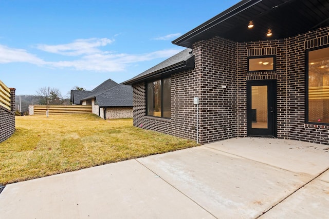 view of side of home featuring brick siding, a patio, fence, and a lawn