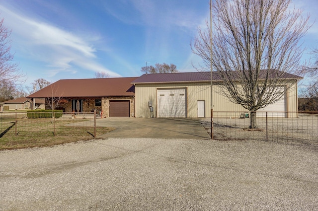 view of front of house with a garage, concrete driveway, metal roof, and fence