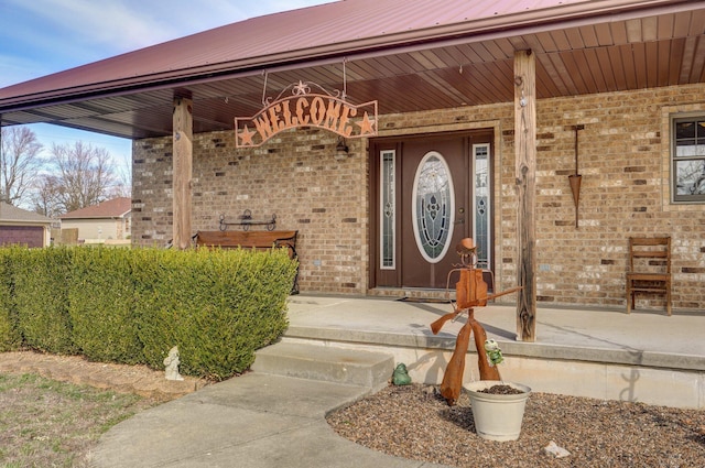 entrance to property featuring covered porch, metal roof, and brick siding