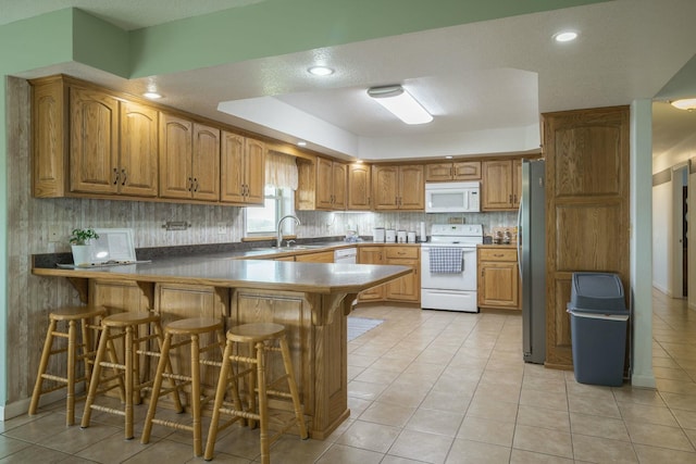 kitchen featuring a breakfast bar area, a peninsula, white appliances, brown cabinets, and tasteful backsplash