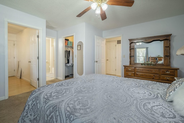 bedroom featuring arched walkways, ceiling fan, ensuite bathroom, carpet, and a spacious closet