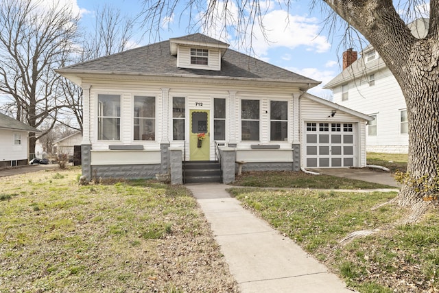 bungalow-style home featuring a garage, entry steps, a shingled roof, and a front lawn