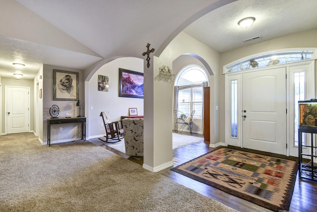 entrance foyer featuring visible vents, vaulted ceiling, a textured ceiling, wood finished floors, and baseboards