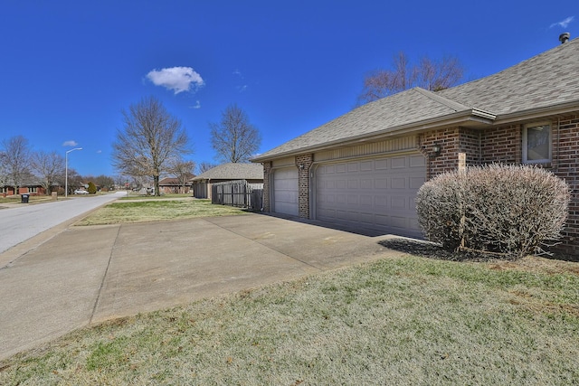 view of property exterior with driveway, a lawn, roof with shingles, fence, and brick siding