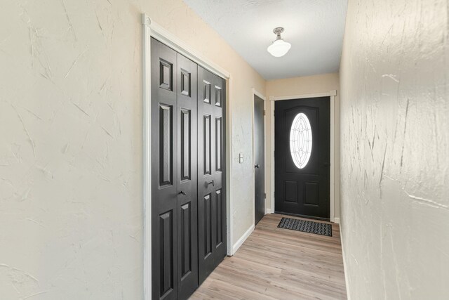 interior space with a textured wall, light wood-style flooring, and baseboards