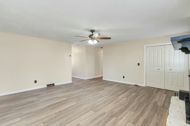 unfurnished living room featuring visible vents, light wood-style flooring, a ceiling fan, a textured ceiling, and baseboards