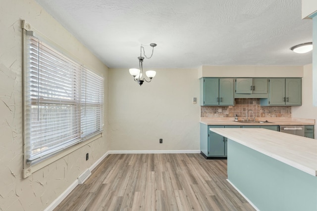 kitchen featuring green cabinetry, a sink, light countertops, light wood-style floors, and backsplash