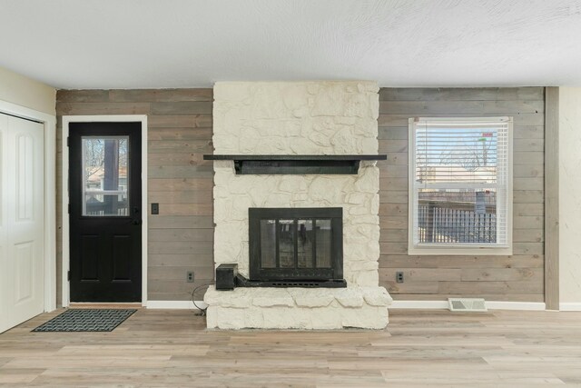 unfurnished living room featuring wooden walls, baseboards, visible vents, wood finished floors, and a fireplace