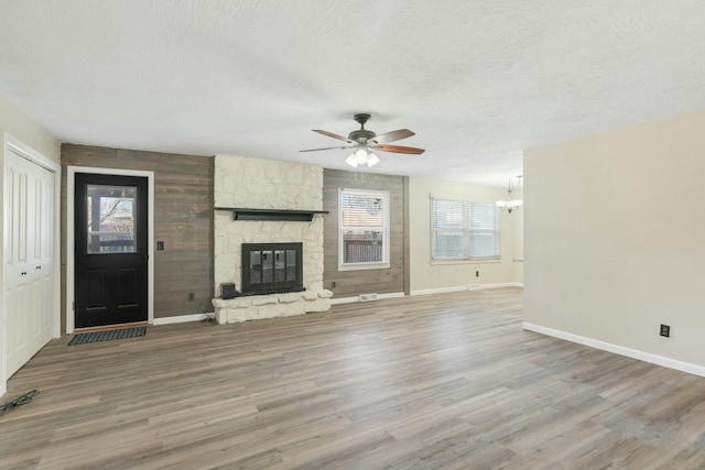 unfurnished living room featuring baseboards, a stone fireplace, a textured ceiling, and wood finished floors
