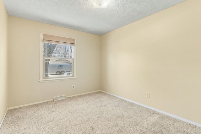 empty room featuring a textured ceiling, carpet flooring, visible vents, and baseboards