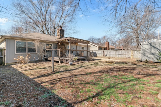 rear view of house featuring a chimney, a deck, a pergola, a fenced backyard, and an outdoor structure