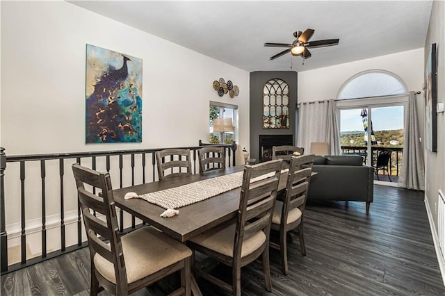 dining area featuring a large fireplace, a ceiling fan, and dark wood-style flooring