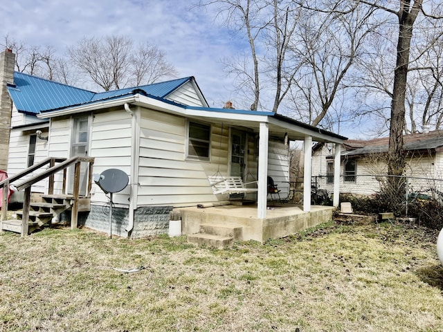 view of front of home with a chimney, a front yard, a patio area, metal roof, and fence