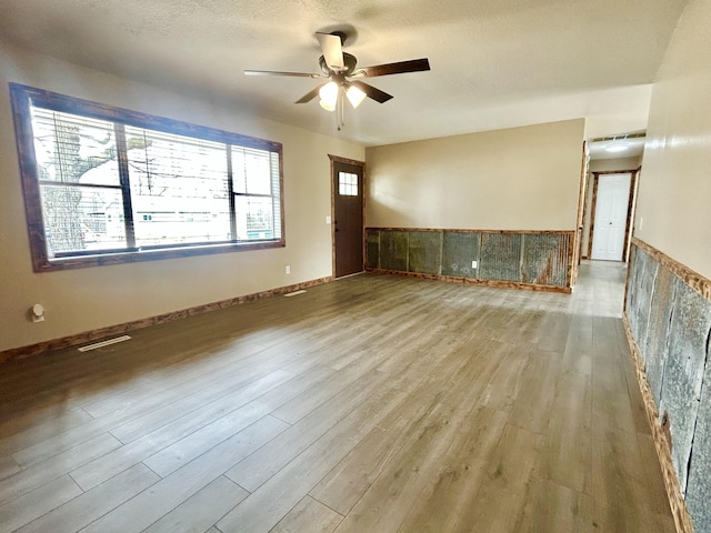 spare room featuring a textured ceiling, wood finished floors, visible vents, baseboards, and a ceiling fan