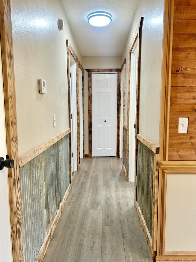 hall featuring a textured ceiling, wood finished floors, and wainscoting