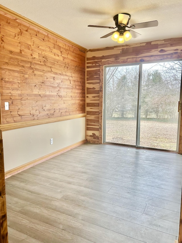 spare room with a textured ceiling, wood finished floors, a ceiling fan, and wooden walls