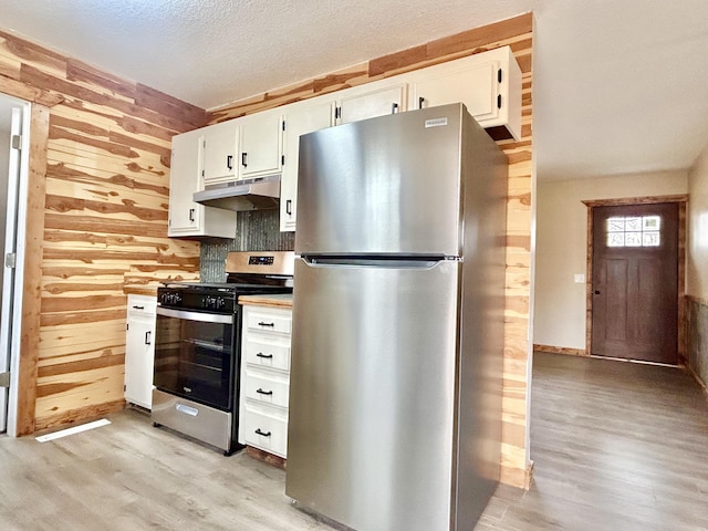 kitchen featuring wooden walls, light wood-style floors, stainless steel appliances, under cabinet range hood, and white cabinetry