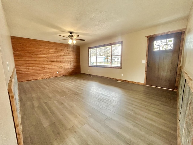 unfurnished living room featuring a textured ceiling, wood walls, wood finished floors, and a ceiling fan