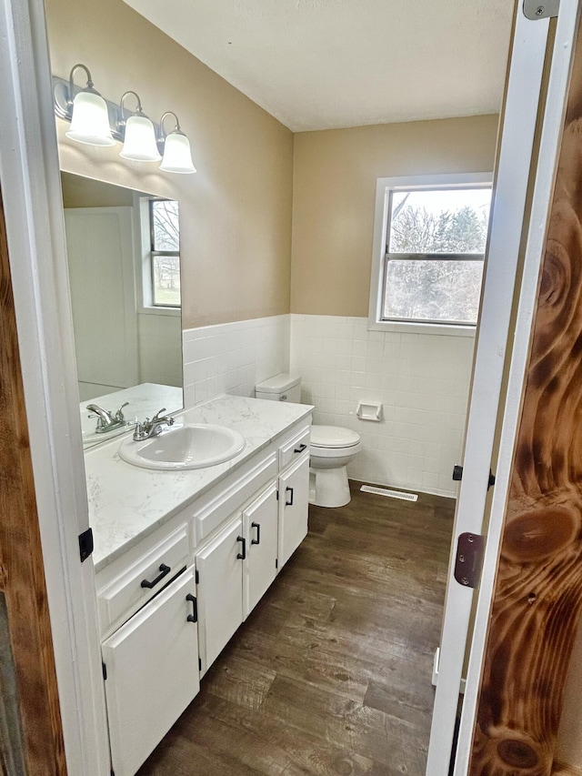 bathroom with toilet, wood finished floors, vanity, tile walls, and wainscoting