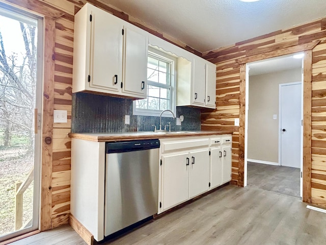 kitchen featuring stainless steel dishwasher, light wood-type flooring, a sink, and wooden walls