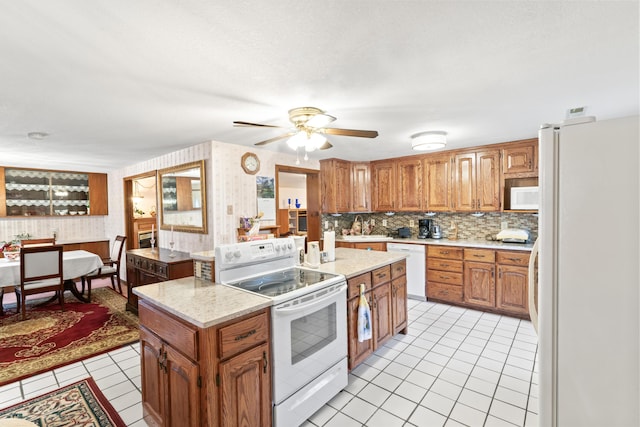 kitchen with light tile patterned floors, white appliances, a center island, tasteful backsplash, and brown cabinetry