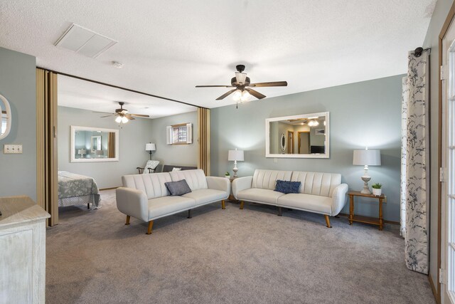 living area featuring carpet floors, visible vents, a textured ceiling, and a ceiling fan