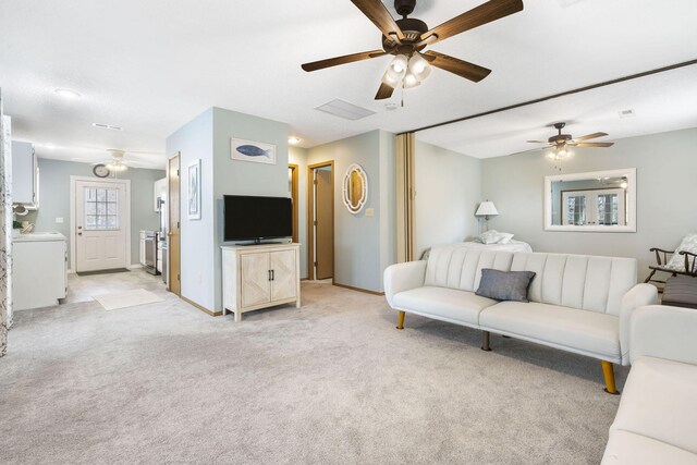 living room featuring light carpet, baseboards, washer / clothes dryer, and a ceiling fan