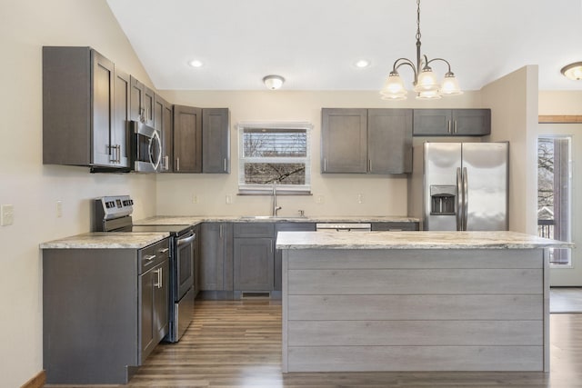 kitchen featuring light stone counters, appliances with stainless steel finishes, wood finished floors, vaulted ceiling, and a sink