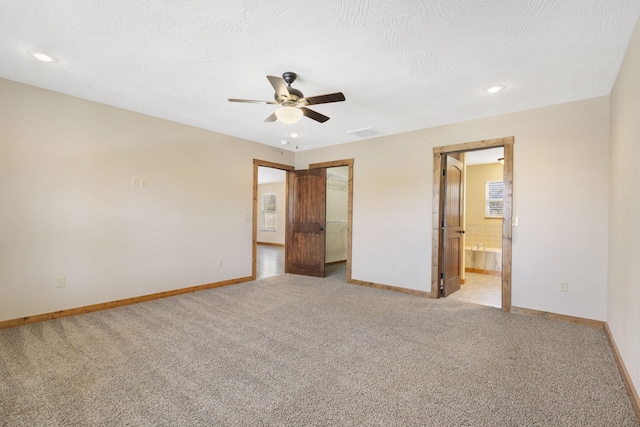 unfurnished bedroom featuring light carpet, baseboards, visible vents, ensuite bathroom, and a spacious closet