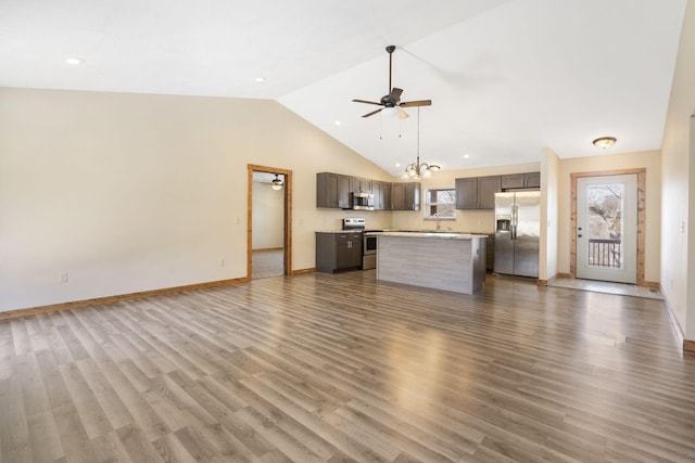 unfurnished living room with ceiling fan with notable chandelier, vaulted ceiling, wood finished floors, and baseboards