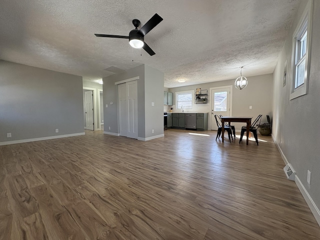 unfurnished living room with dark wood finished floors, visible vents, a sink, a textured ceiling, and baseboards